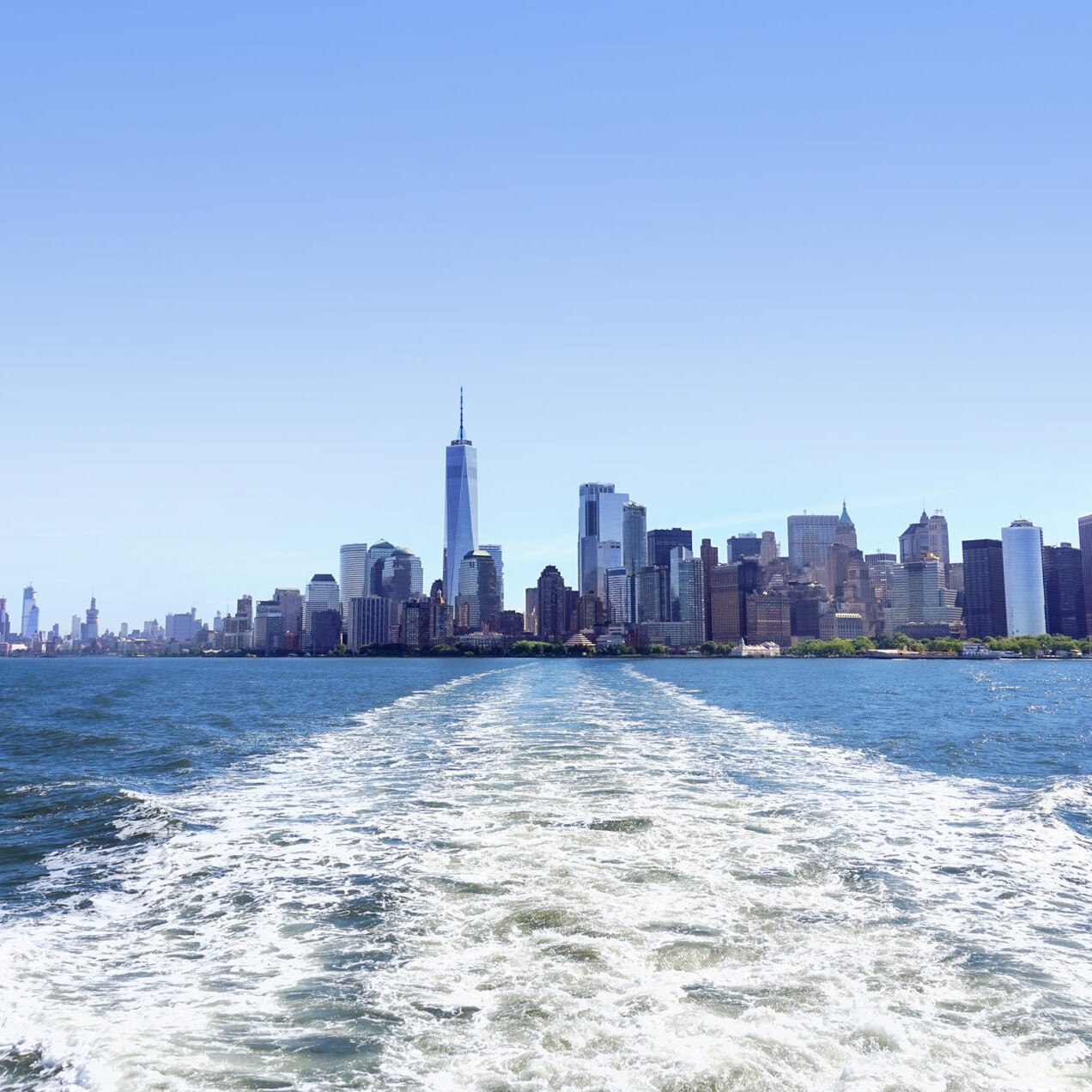 Lower Manhattan view from cruise ship or yacht with the flag of the United States of America in New York. Scenic view to NY Downtown and city centre. Staten Island Ferry. Tourists cruising in boat.